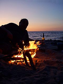 Mann, Silhouette, am Strand mit Lagerfeuer nach dem Sonnenuntergang