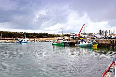 Fischereihafen mit bleiern glitzerndem Wasser und bunten Fischerbooten