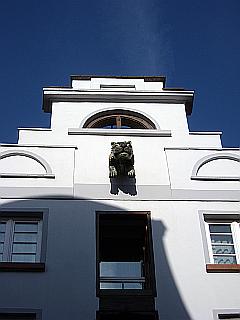 alter Giebel mit Löwenkopf - weiße Fassade vor blauem Himmel